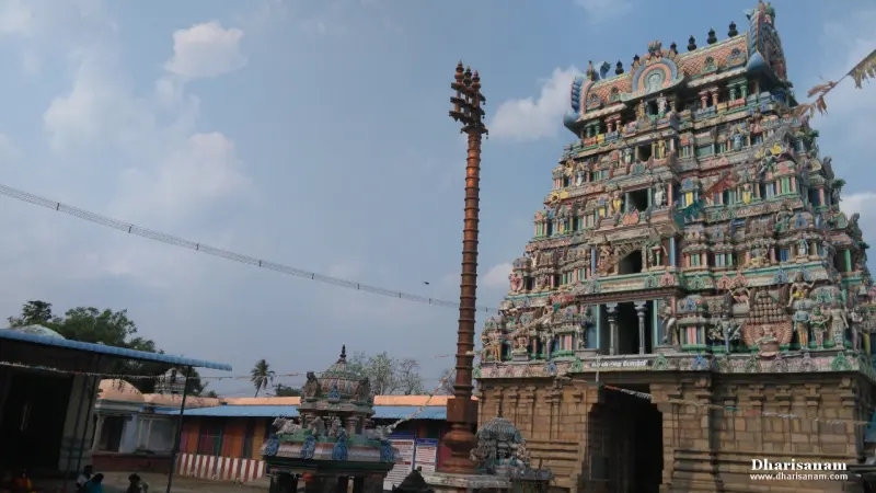 A tall tower covered in painted figures beside a tall flagstaff in the temple courtyard, with small shrines below