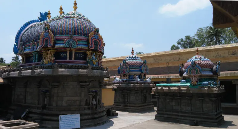 Brightly painted shrine domes on stone bases in an open courtyard, with the Rajagopuram rising behind