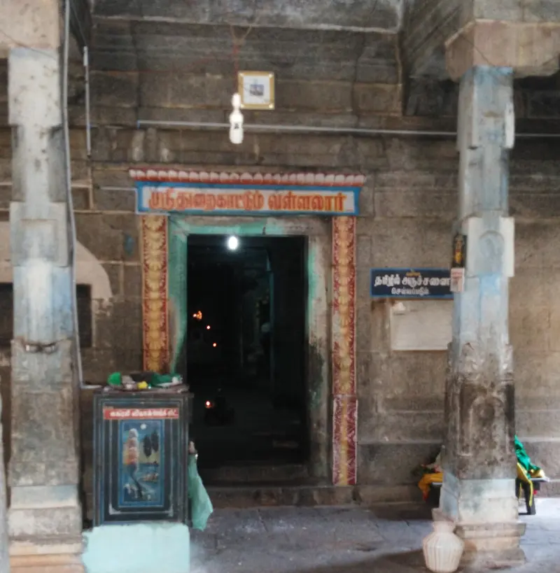 A dark stone doorway between pillars, with a Tamil name board above it and lamps glowing inside.