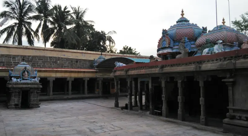 Wide stone courtyard with a small shrine on the left and two domed roofs above the corridor on the right