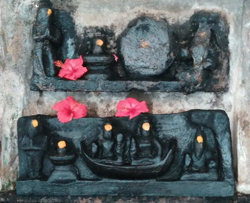 An old stone relief of a boat scene adorned with red flowers
