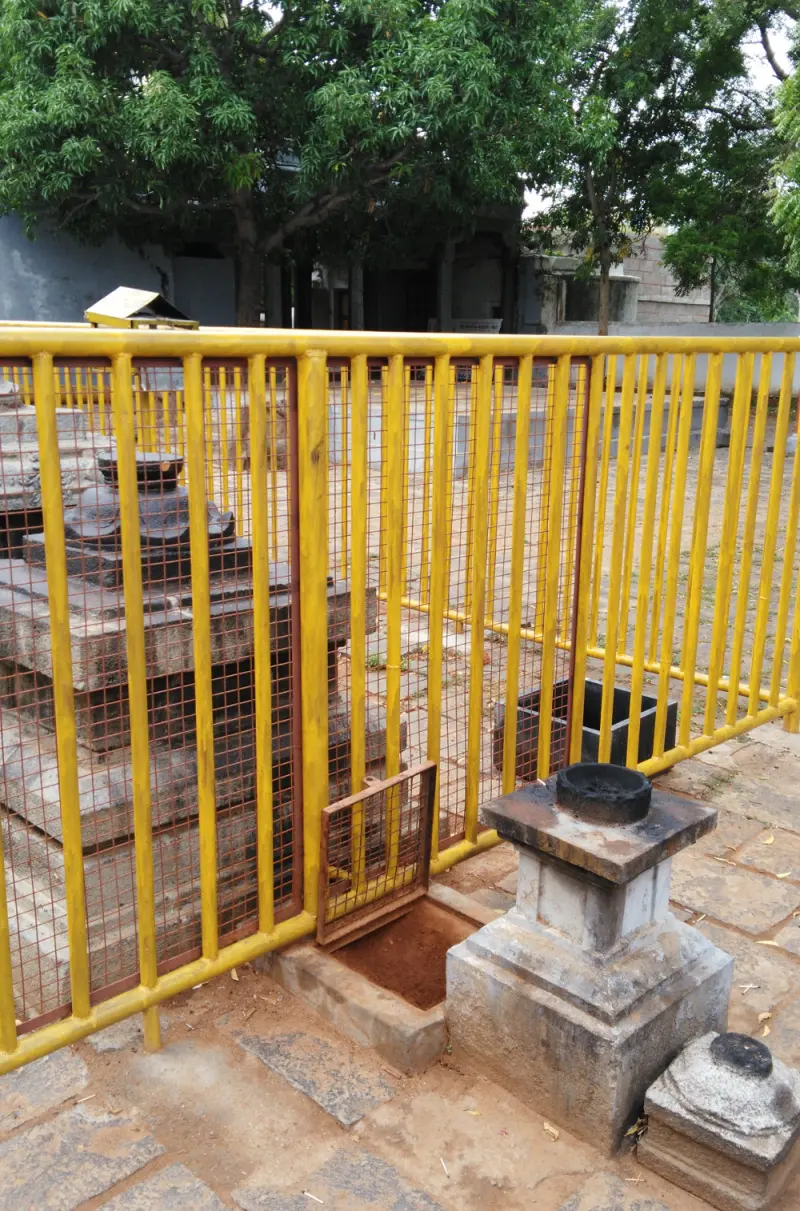 A small stone pedestal and stepped stone base beside a yellow railing, with a pit in the paving.