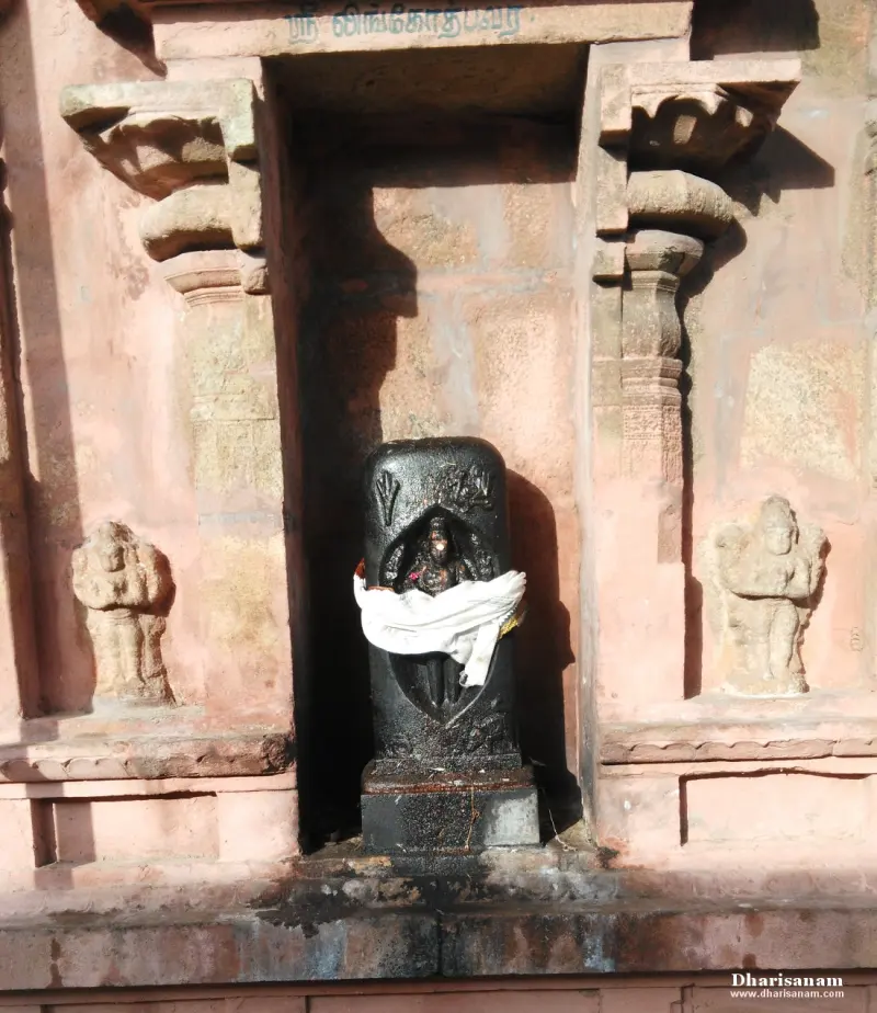 A dark stone lingam form with a white cloth, set in a niche between carved pilasters.