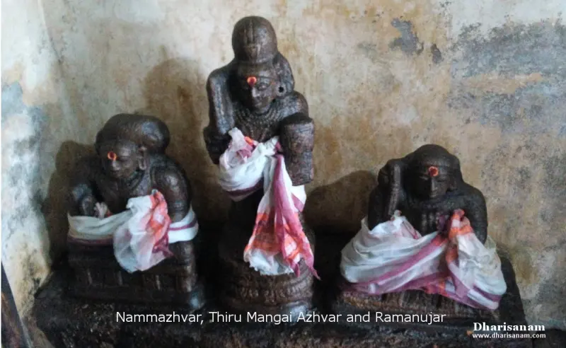 Three dark stone idols with red marks on their foreheads, wrapped in white cloth with red borders; a caption names them