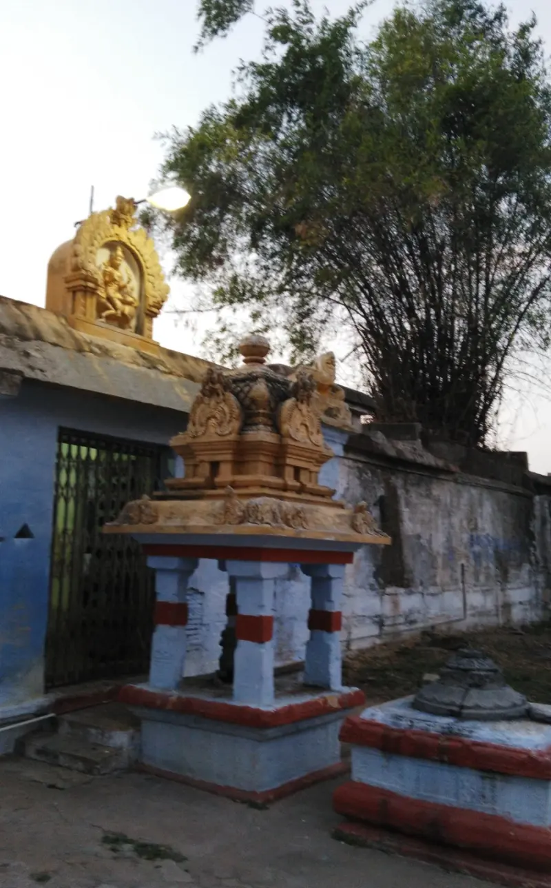A small pillared stone shrine with red and blue bands, with a tall bamboo clump and a temple wall behind.