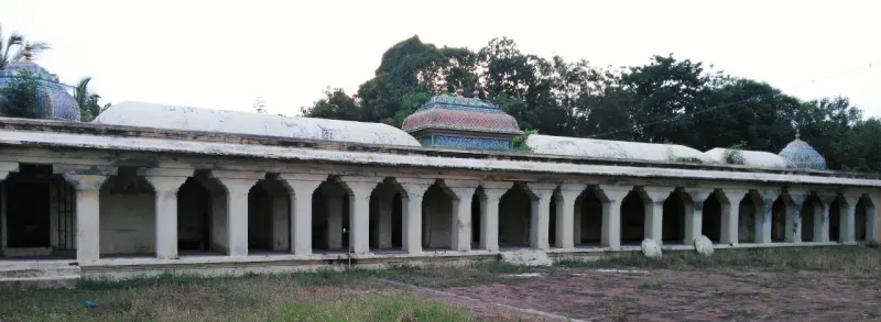 A long open corridor of white arches and pillars, with domed shrine tops rising behind it.