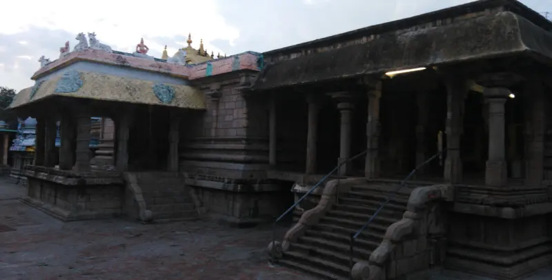 A stone pillared hall with a wide flight of steps at dusk, and a smaller painted hall at the left.