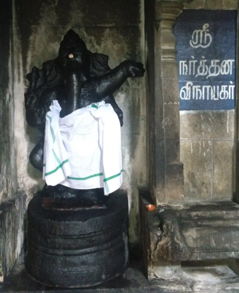 A dancing Vinayakar in dark stone on a round base, with a Tamil name board
