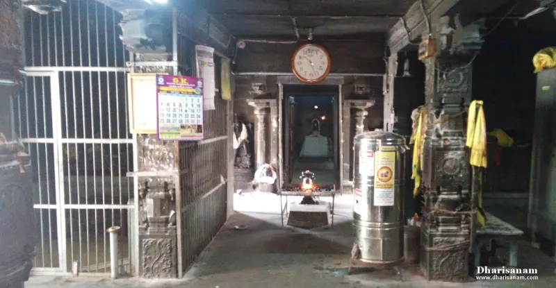 A dim stone hall with a lit lamp in the centre and a doorway leading to the sanctum beyond