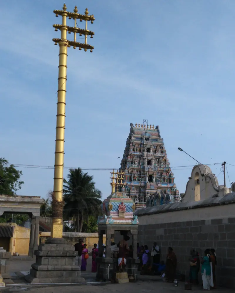 A tall golden flagstaff beside a small pavilion, with a painted tower in the distance