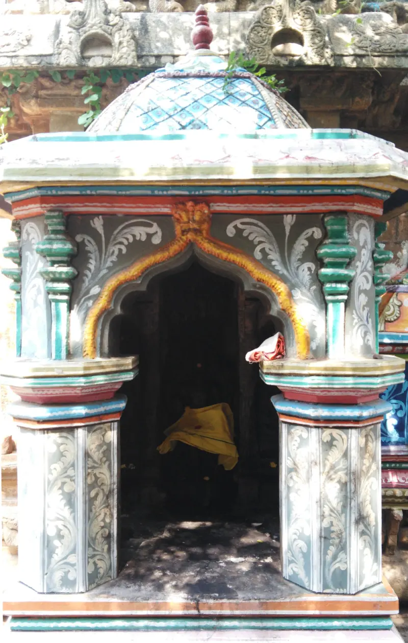 Small painted shrine with a domed roof and an arched opening holding a figure draped in yellow cloth