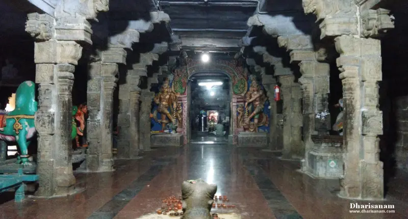 A dim stone hall of carved pillars, a Nandi in the foreground and guardian figures at the far doorway