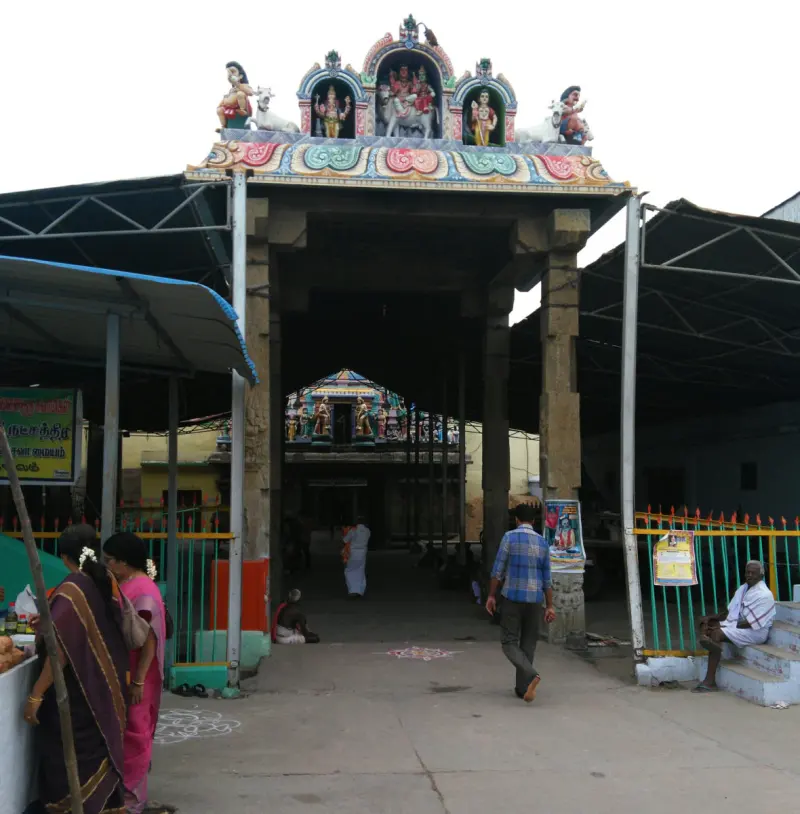 A stone-pillared gateway topped with painted figures and bulls, with people walking in