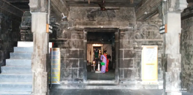 A stone doorway with steps at the left, through which a devotee and a lit shrine can be seen.