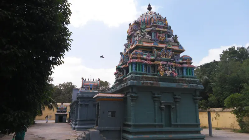 A tiered painted shrine tower above grey stone walls, with trees on both sides and a yellow compound wall