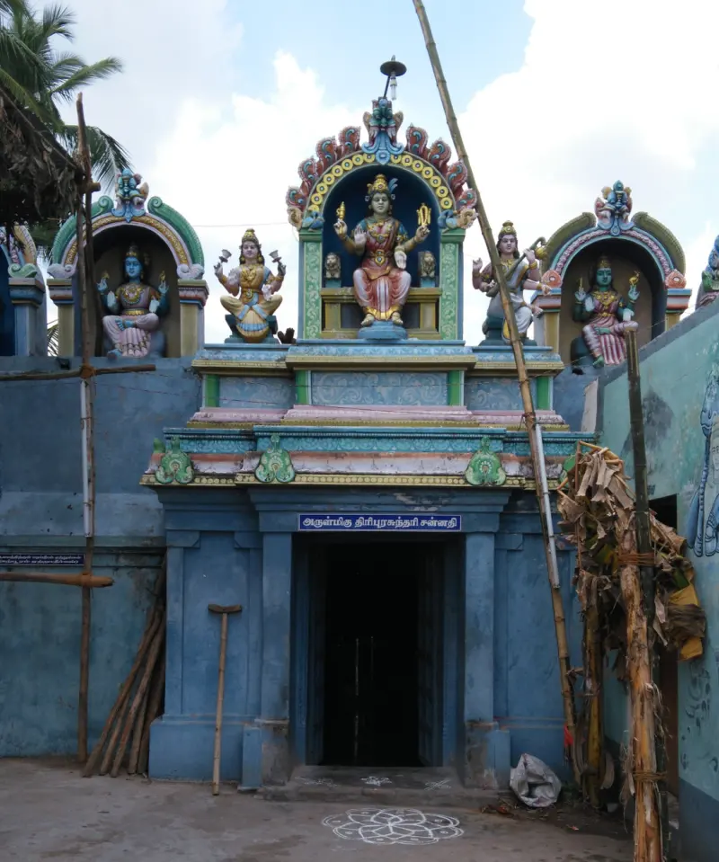 Blue shrine doorway topped by a seated goddess figure, with a rangoli on the floor