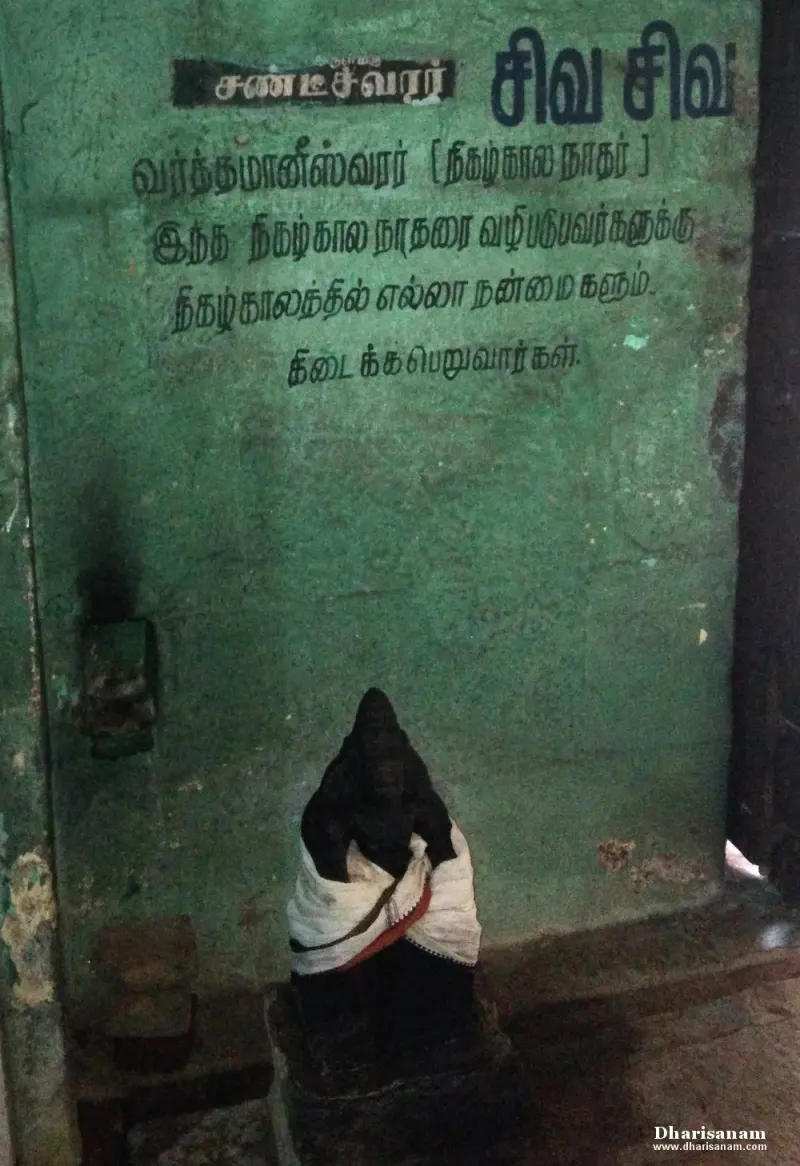 A small dark figure in white cloth below a green wall painted with Tamil lines