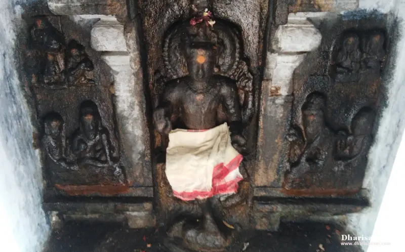 A dark stone idol in a white and red cloth, with carved figure panels on both sides