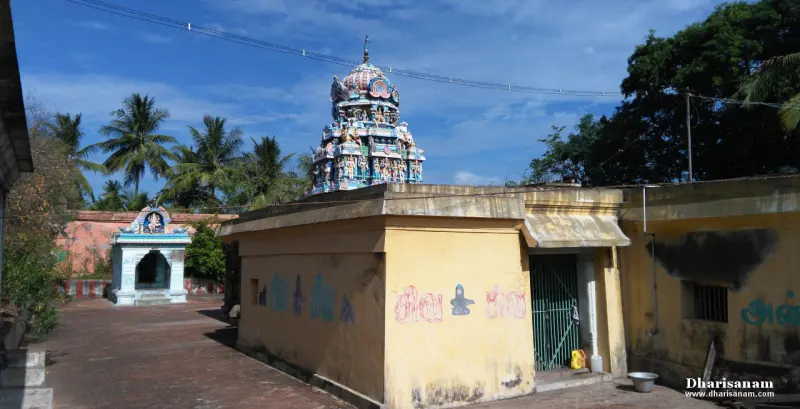 A yellow-walled building with a green door, a painted tower behind it and a small shrine at the left