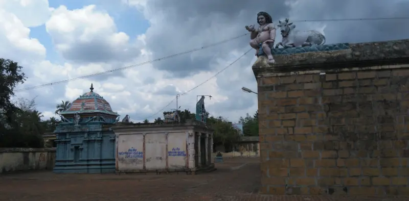 A domed shrine and a small hall seen past a brick wall topped with a bull and figure