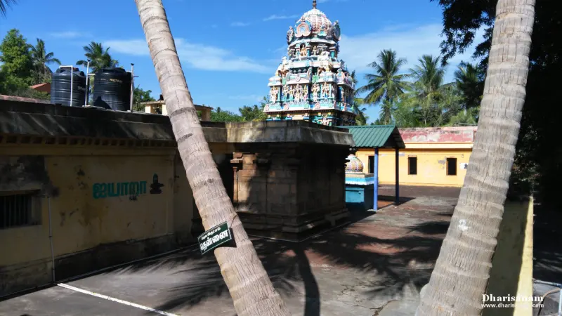 A colourful tower rising behind a stone shrine and a courtyard, with two coconut trunks in the foreground