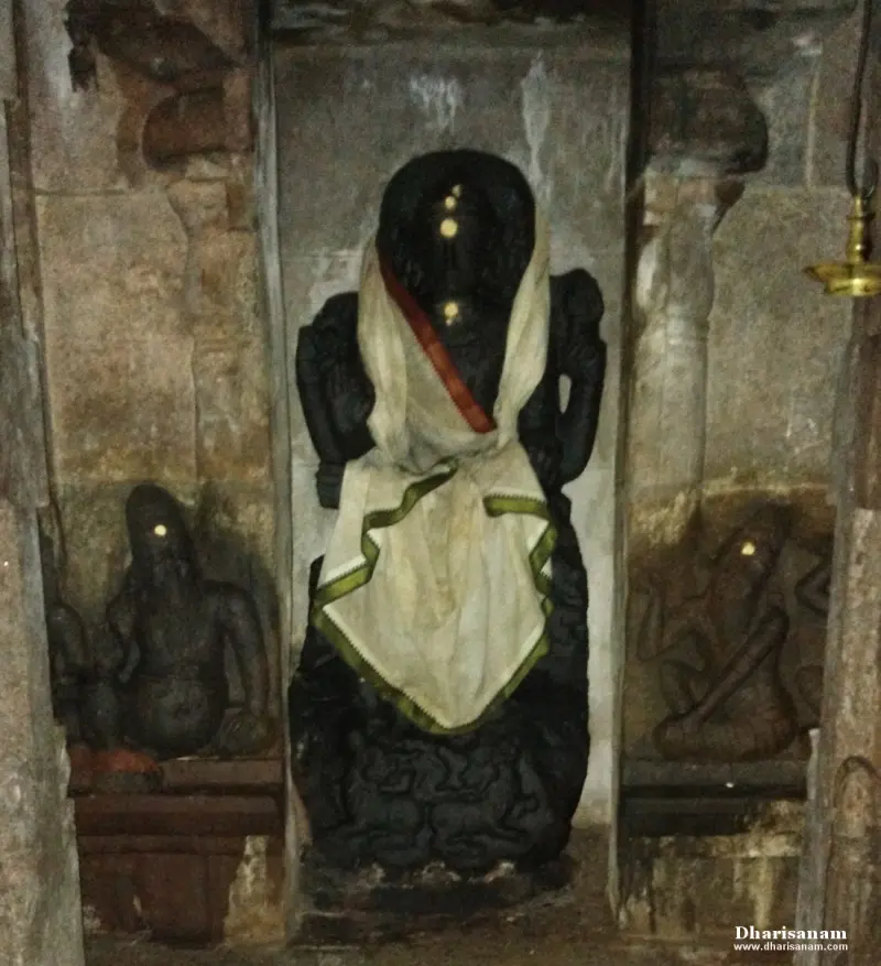 A black stone idol in a wall niche wearing a white cloth, with a smaller figure on each side