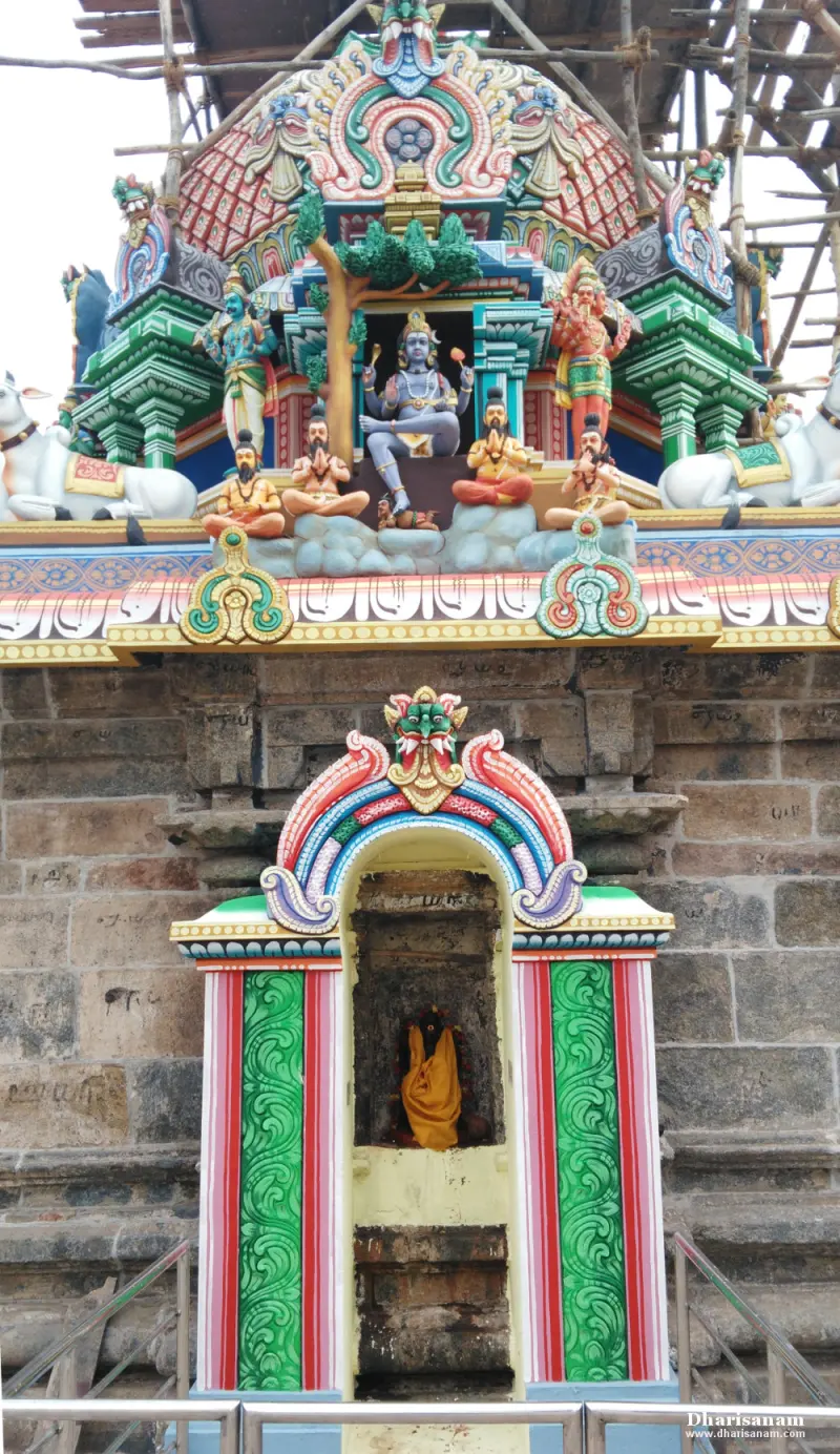 A colourful shrine tower with seated figures, above a small niche with a figure in yellow cloth