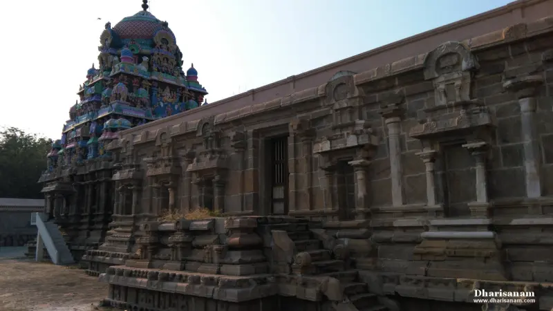 Long weathered stone wall of the corridor with pilasters, and a painted tower at the far left