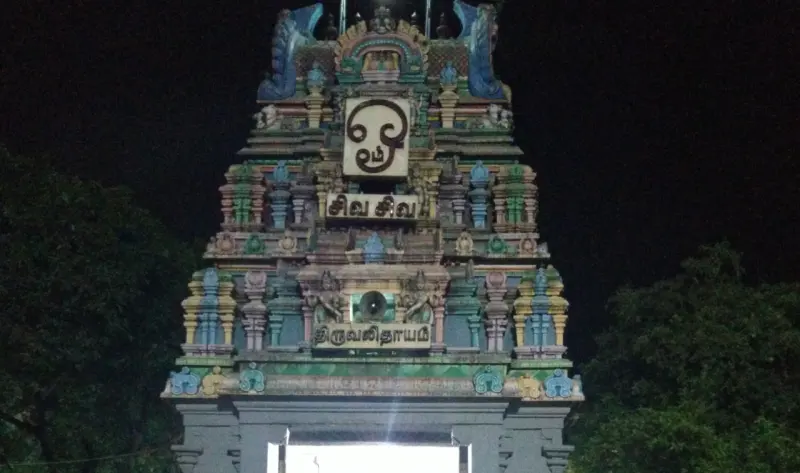 A colourful tiered temple tower lit against a night sky, with the name Thiruvalithayam in Tamil on a board