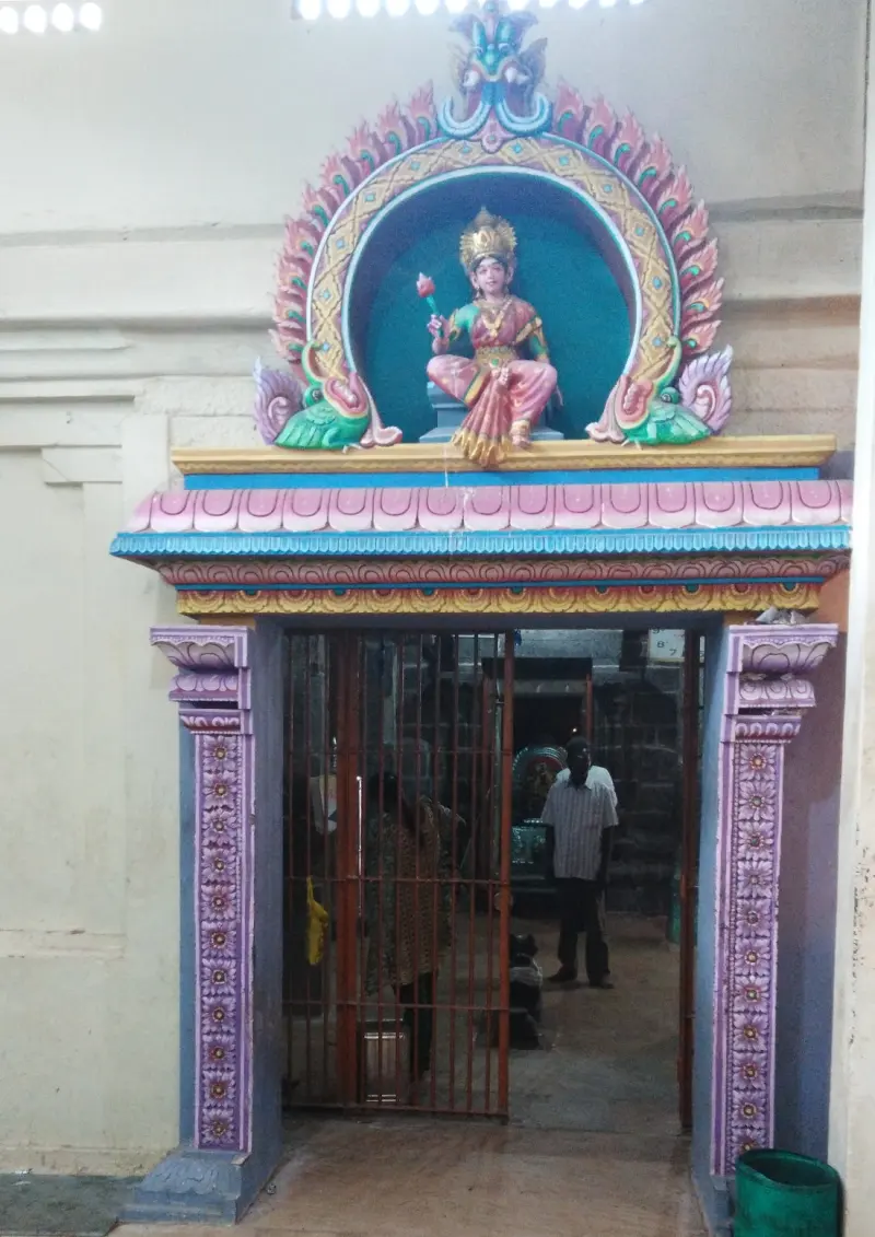 A painted seated goddess holding a lotus above a barred doorway with purple pillars; a man stands inside.