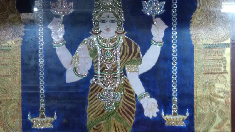 A painted four-armed goddess in a green and gold sari, with lotus flowers in her upper hands.