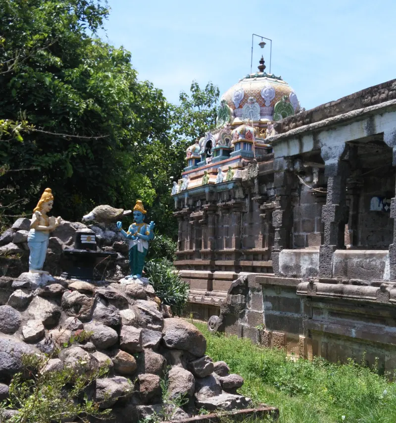 A domed shrine tower beside a pillared hall; in front, two painted figures and a small lingam on a pile of rocks.