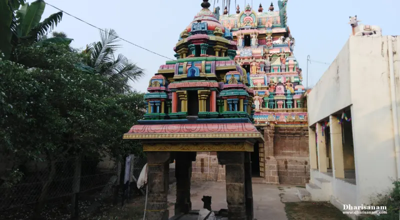Painted multi-tier tower with sculptures beside a stone mandapa