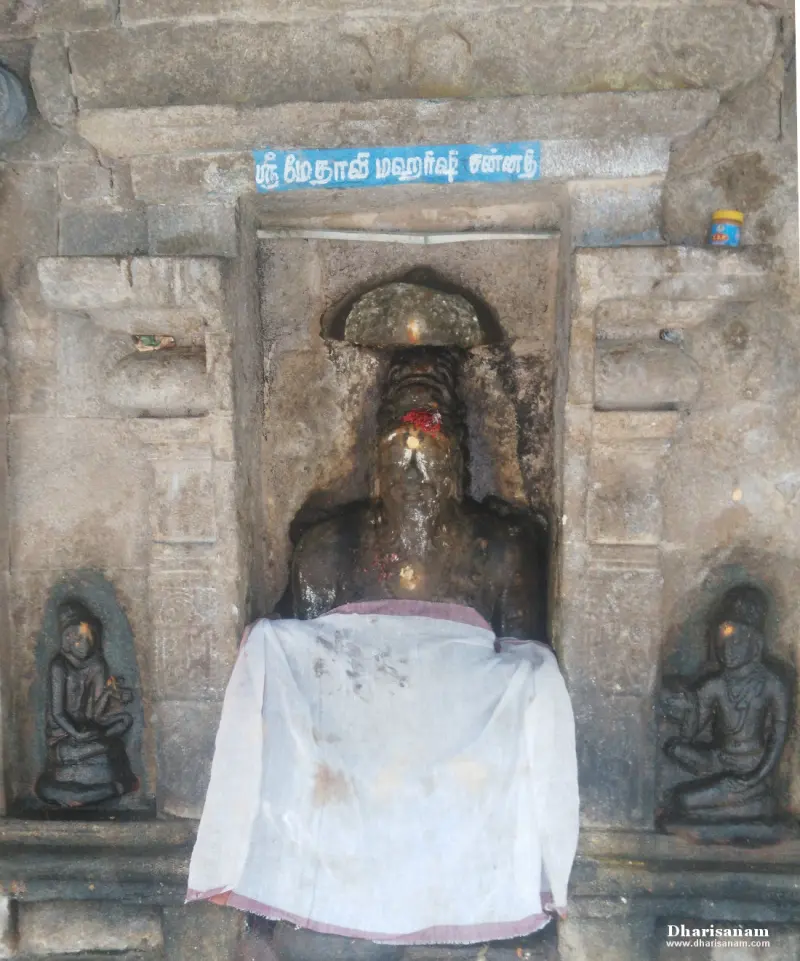 Black stone idol of a bearded sage in a niche, with a Tamil name board above