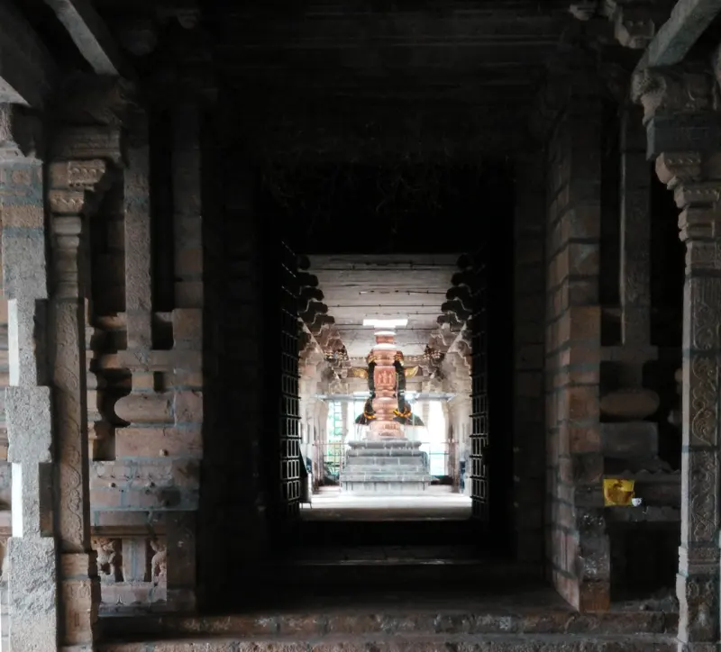 A long dark pillared corridor with a lit shrine visible at the far end