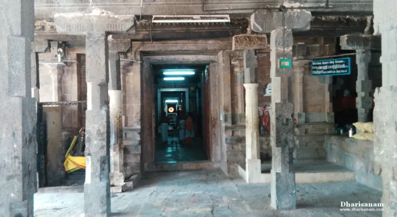 A stone hall with pillars and a lit doorway at the centre, where devotees stand in the passage beyond