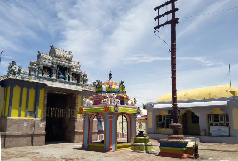 Open courtyard with a tall flagstaff, a small painted shrine and a tower on the left