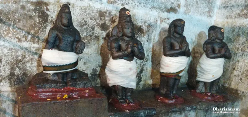Four dark stone idols in white cloth on a low stone shelf against a wall