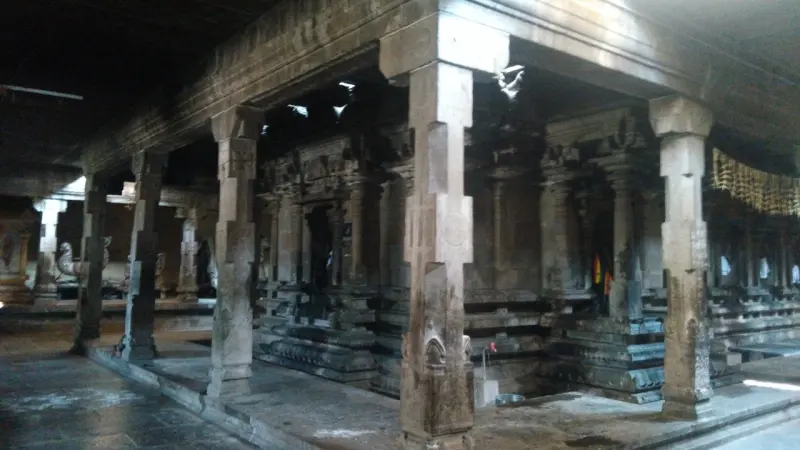 A dim stone hall with tall square pillars and carved shrine fronts beyond them