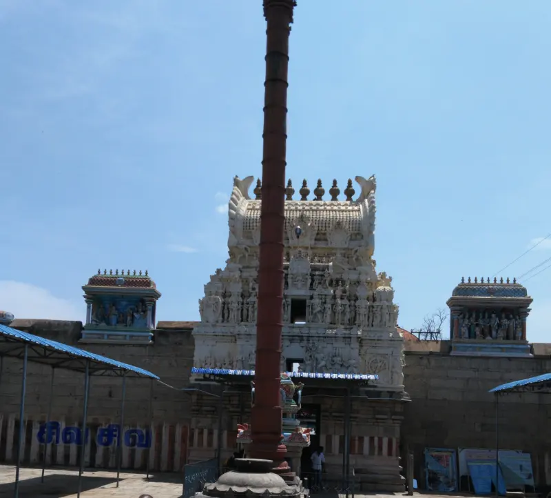 A tall dark flagstaff in front of a white gateway tower, with two small painted towers on the wall