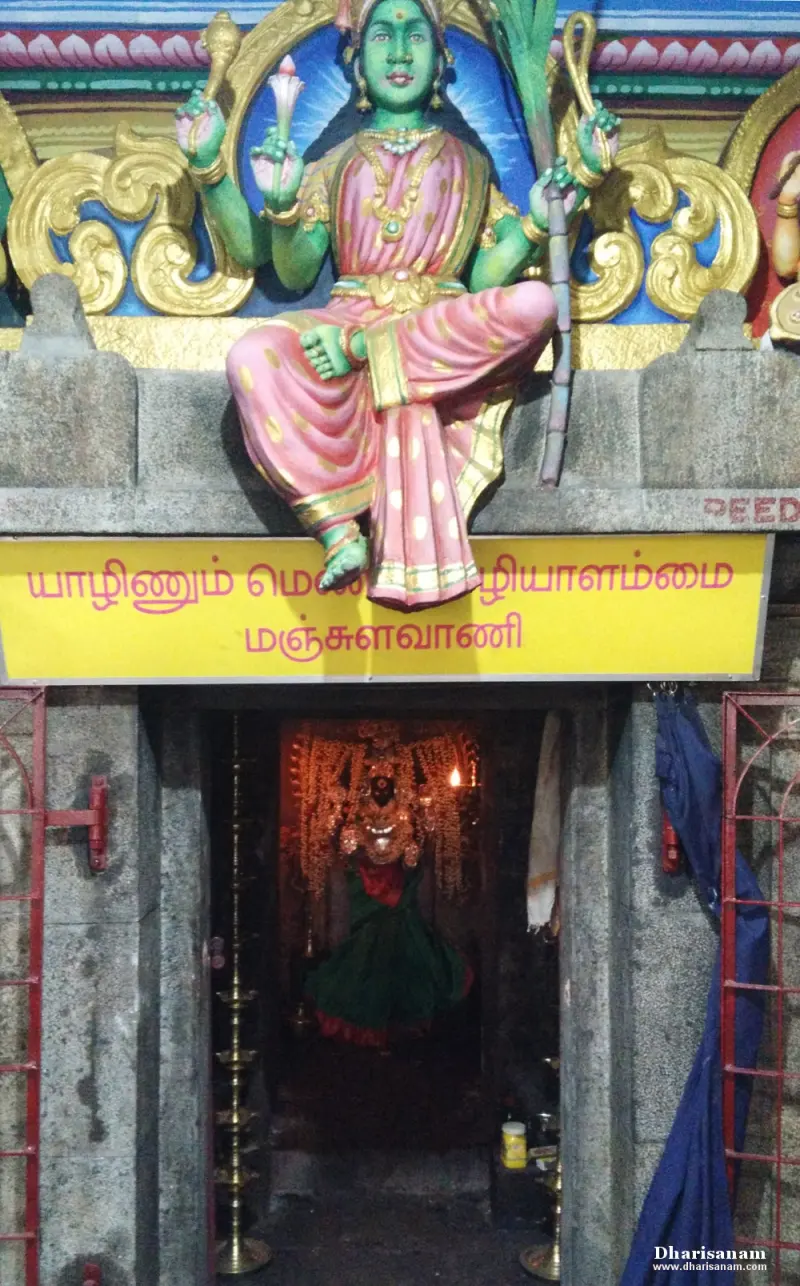 A shrine entrance with a painted goddess seated above a yellow Tamil name board, and a lit image inside