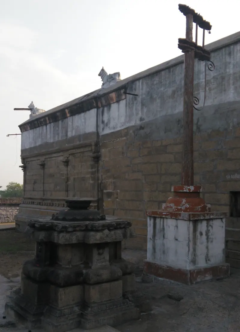 A tall flagstaff on a whitewashed base and a carved stone altar beside a stone wall