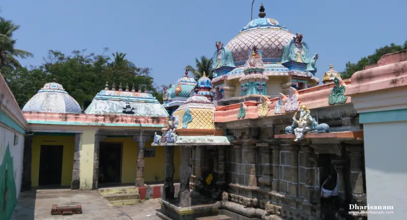 Domed shrine roofs and a painted stucco tower rise above a pillared stone corridor under a clear sky