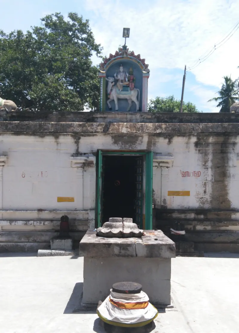A shrine entrance with a painted relief of Shiva and Parvathi on a bull above, and a Nandi base and stand in front.