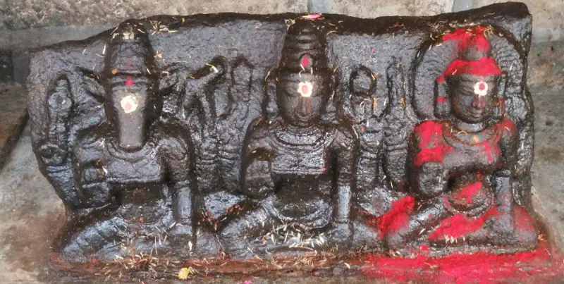 A dark granite slab carved with three seated figures, marked with a dot on each forehead