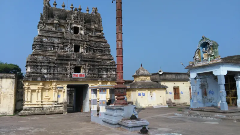 A dark stone tower on a yellow base beside a tall red flagstaff, with a blue shrine at the right.