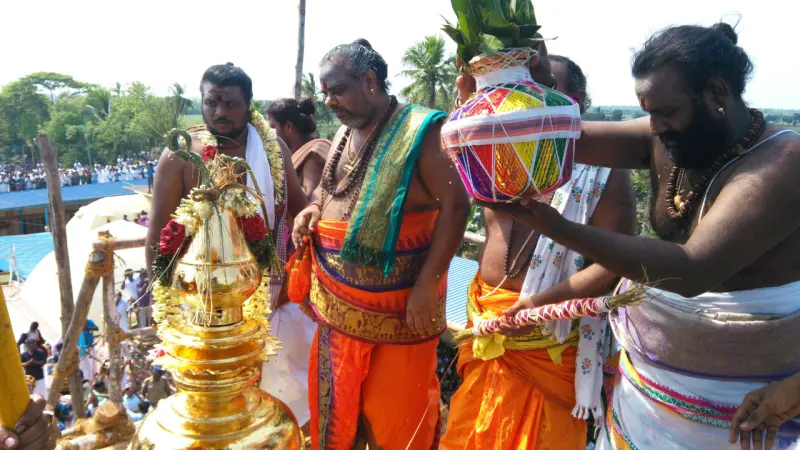 Priests in orange and saffron cloth hold a gilded kalasam and a pot wrapped in colourful netting.