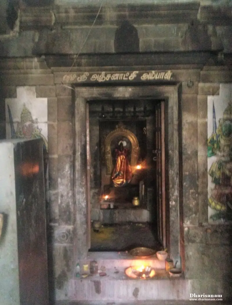 A narrow doorway with a Tamil name board above it leads to a lit shrine, with painted guardians on the walls beside