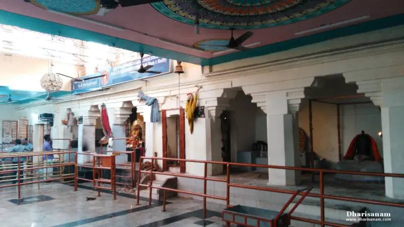 A pillared hall with railings, a decorated shrine at the left and an idol in red cloth at the right