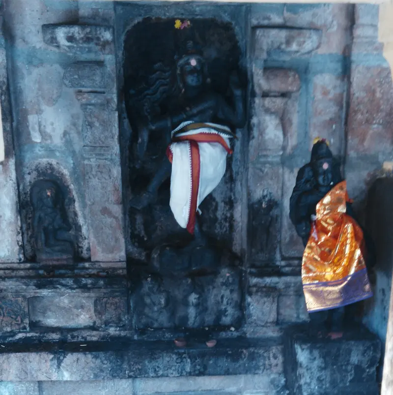 A carved dark stone figure in a wall niche, with a smaller idol in orange cloth beside it.